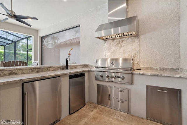 kitchen featuring wall chimney exhaust hood, refrigerator, light stone counters, and ceiling fan