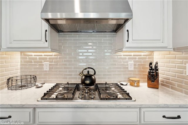 kitchen featuring decorative backsplash, light stone countertops, wall chimney exhaust hood, white cabinetry, and stainless steel gas stovetop