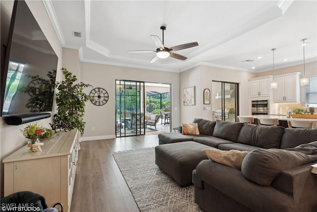 living room featuring ceiling fan, a raised ceiling, ornamental molding, and dark wood-type flooring