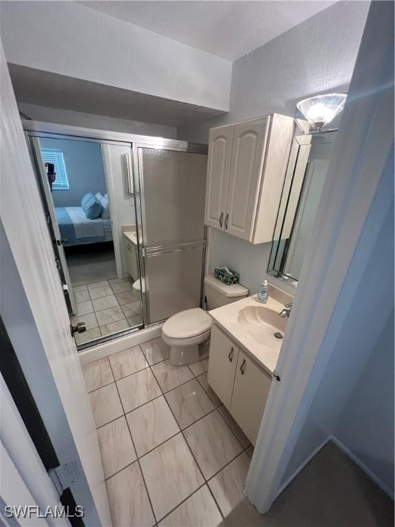 bathroom with tile patterned flooring, vanity, a shower with door, and toilet