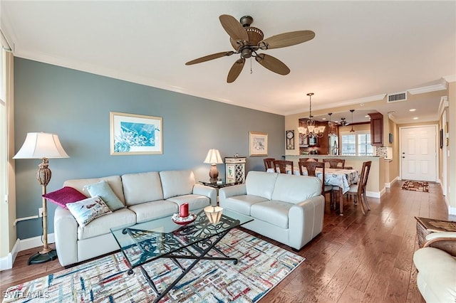 living area with dark wood-type flooring, visible vents, ornamental molding, and baseboards