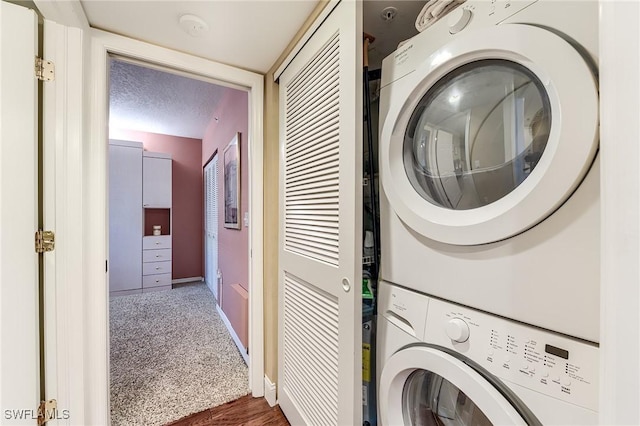 laundry area featuring laundry area, baseboards, stacked washer / dryer, dark colored carpet, and a textured ceiling