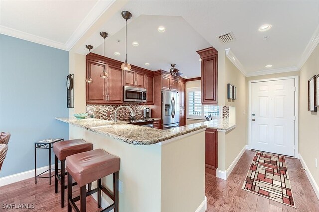 kitchen with light stone countertops, kitchen peninsula, decorative light fixtures, appliances with stainless steel finishes, and ornamental molding