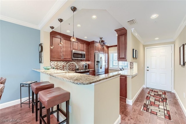 kitchen with light stone counters, stainless steel appliances, a peninsula, brown cabinets, and pendant lighting