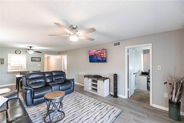 living room with ceiling fan, light hardwood / wood-style floors, and a textured ceiling