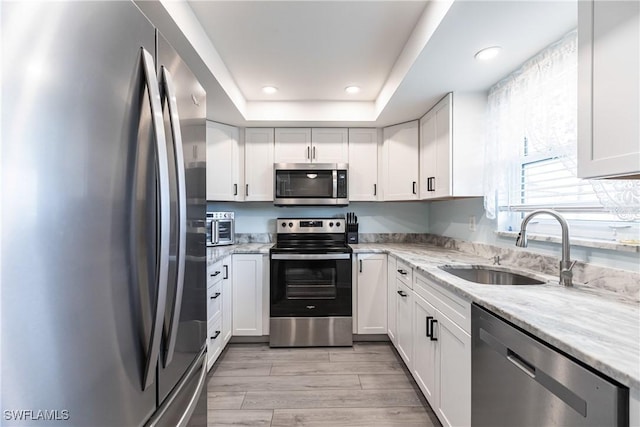 kitchen featuring white cabinets, sink, appliances with stainless steel finishes, a tray ceiling, and light stone counters