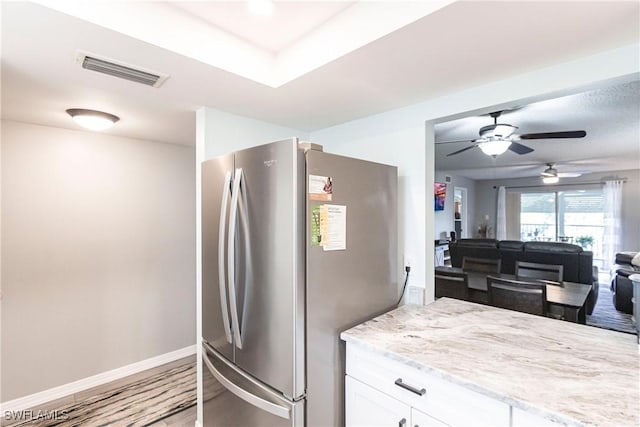 kitchen with white cabinets, light hardwood / wood-style floors, light stone counters, and stainless steel refrigerator