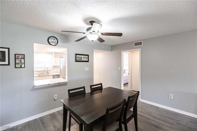 dining room with ceiling fan, sink, dark wood-type flooring, and a textured ceiling