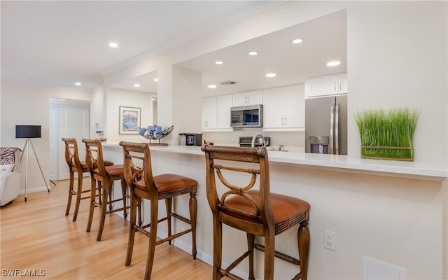 kitchen with a kitchen breakfast bar, kitchen peninsula, light hardwood / wood-style floors, white cabinetry, and stainless steel appliances