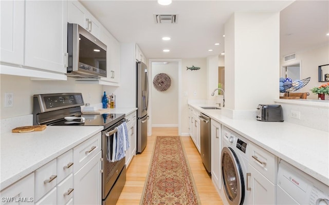 kitchen featuring sink, appliances with stainless steel finishes, light hardwood / wood-style floors, white cabinetry, and washer / clothes dryer