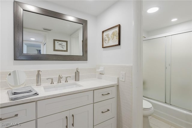 full bathroom featuring vanity, combined bath / shower with glass door, tile patterned flooring, toilet, and tile walls