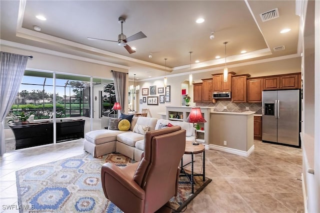 living room with ceiling fan with notable chandelier, a tray ceiling, and crown molding