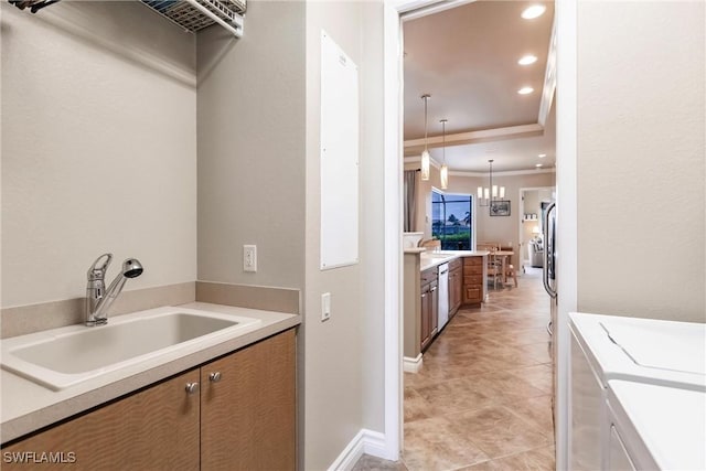 clothes washing area featuring washing machine and dryer, ornamental molding, sink, and a chandelier