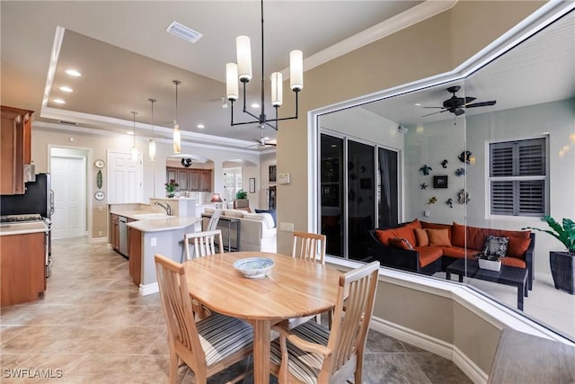 tiled dining area with ceiling fan with notable chandelier, a tray ceiling, crown molding, and sink