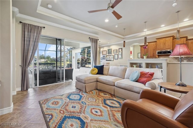 living room with a raised ceiling, crown molding, light tile patterned flooring, and ceiling fan