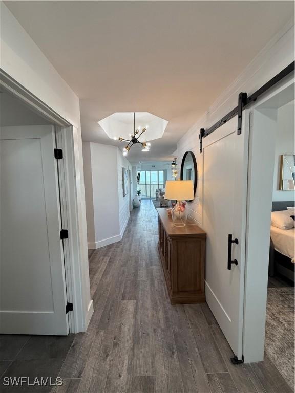 hall featuring dark hardwood / wood-style floors, a barn door, and an inviting chandelier