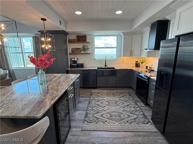 kitchen featuring white cabinetry, sink, beverage cooler, black appliances, and wall chimney range hood