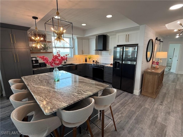 kitchen with hardwood / wood-style floors, decorative light fixtures, black appliances, a barn door, and wall chimney exhaust hood