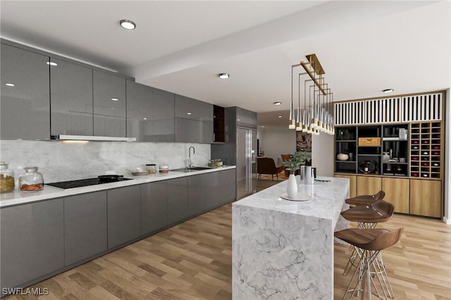 kitchen with a breakfast bar, black electric stovetop, sink, hanging light fixtures, and gray cabinets