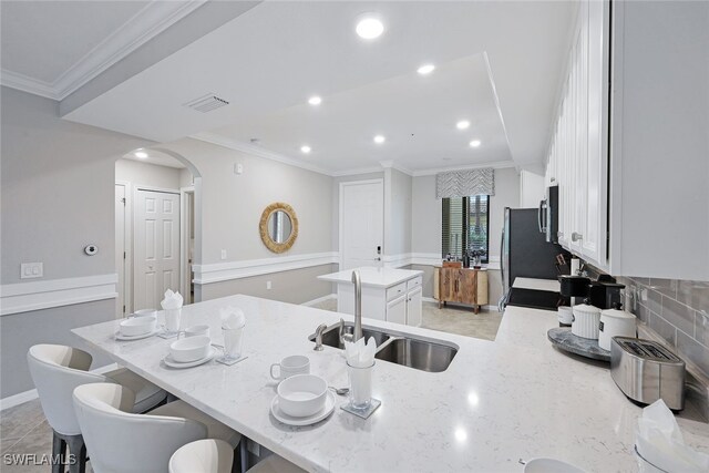 kitchen featuring sink, a breakfast bar, white cabinetry, light stone counters, and a kitchen island