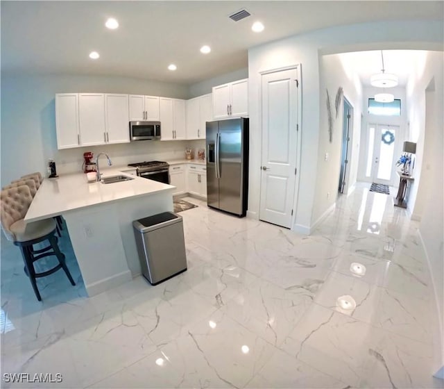 12830 Hawkins Dr, Estero, FL 33928 - kitchen featuring appliances with stainless steel finishes, a peninsula, light marble finish floors, a breakfast bar, and light countertops