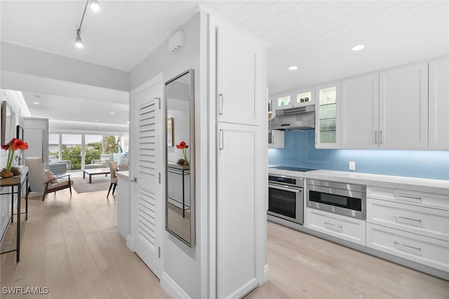 kitchen with built in microwave, white cabinetry, rail lighting, oven, and light hardwood / wood-style floors