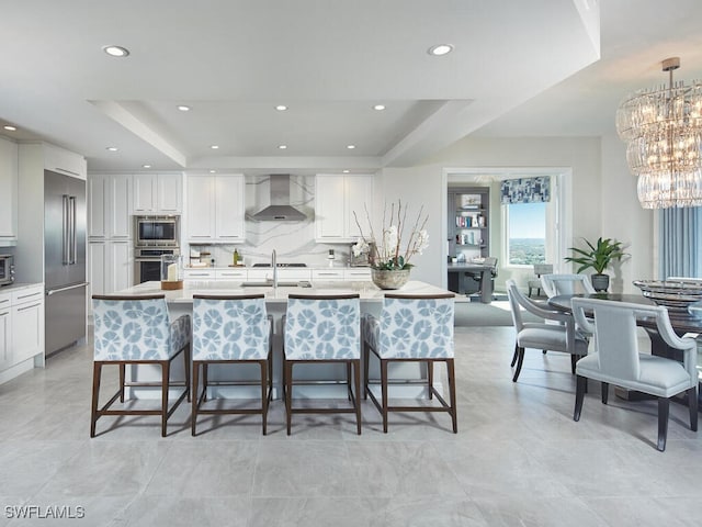 kitchen featuring built in appliances, a tray ceiling, hanging light fixtures, and wall chimney exhaust hood