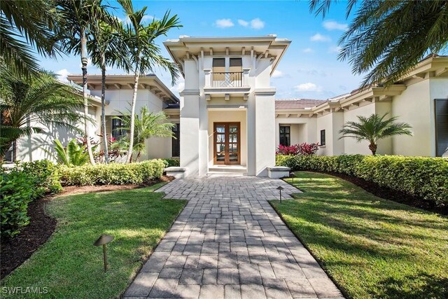 view of front of property featuring a front lawn, a balcony, and french doors