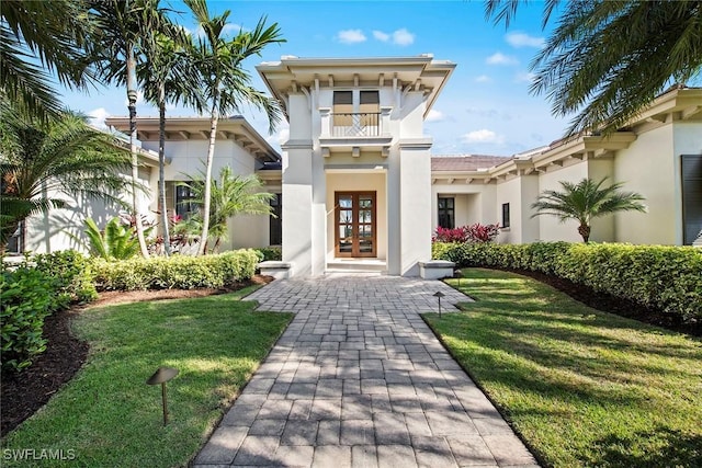 view of front of house featuring french doors, a front lawn, a balcony, and stucco siding