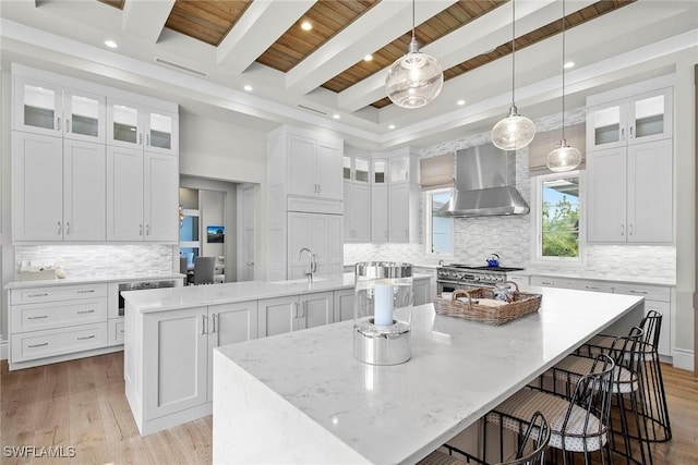 kitchen with white cabinets, a large island with sink, and wall chimney exhaust hood