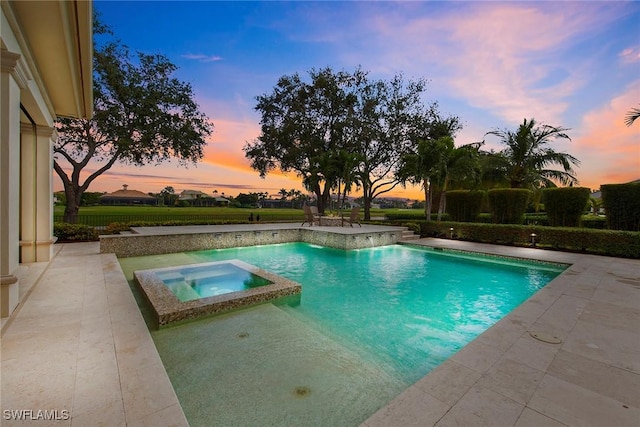 pool at dusk featuring an in ground hot tub and a patio area