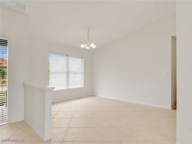 tiled spare room featuring a wealth of natural light and a chandelier