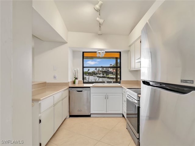 kitchen with sink, rail lighting, appliances with stainless steel finishes, white cabinets, and light tile patterned flooring