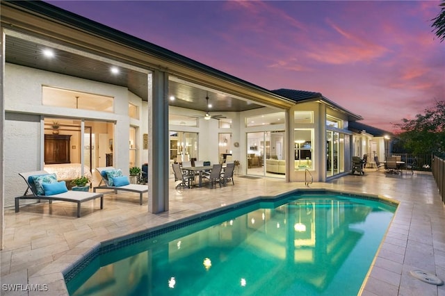 pool at dusk featuring outdoor lounge area, ceiling fan, and a patio