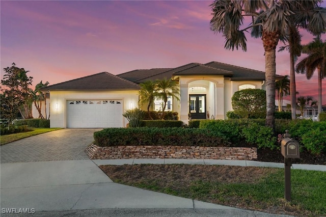 view of front of property with an attached garage, stucco siding, decorative driveway, french doors, and a tiled roof