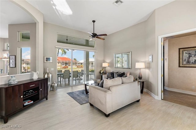 living room featuring a towering ceiling, light hardwood / wood-style floors, and ceiling fan