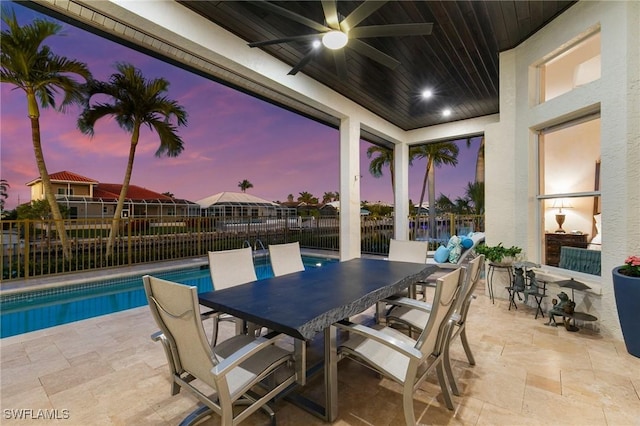 patio terrace at dusk featuring a fenced in pool and ceiling fan