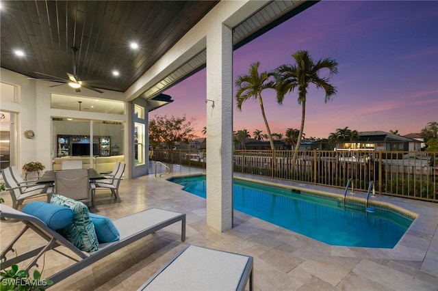 pool at dusk featuring ceiling fan and a patio area