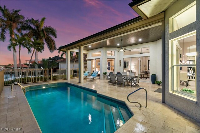 pool at dusk featuring ceiling fan and a patio area