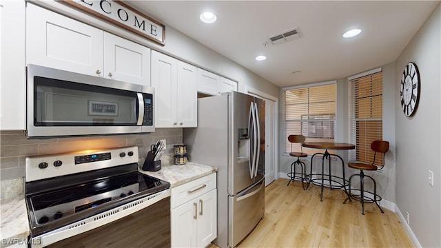 kitchen with white cabinets, light hardwood / wood-style flooring, light stone countertops, appliances with stainless steel finishes, and tasteful backsplash