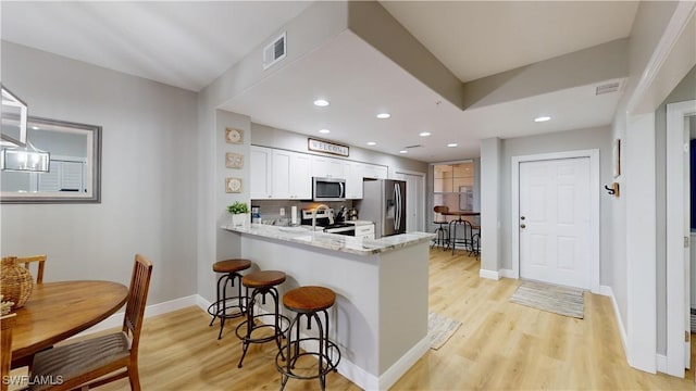 kitchen with backsplash, white cabinets, light wood-type flooring, appliances with stainless steel finishes, and kitchen peninsula