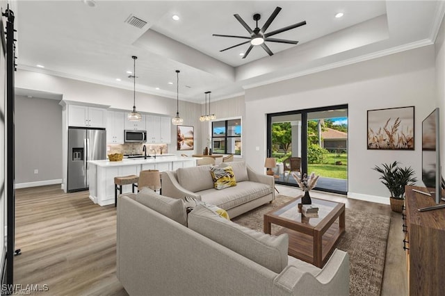 living room featuring a raised ceiling, sink, crown molding, ceiling fan, and light hardwood / wood-style floors