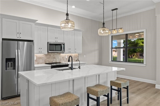 kitchen featuring a center island with sink, appliances with stainless steel finishes, decorative light fixtures, light stone counters, and white cabinetry