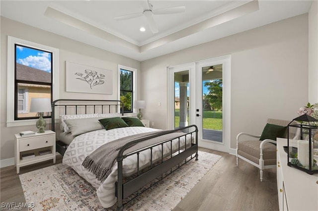 bedroom with ceiling fan, wood-type flooring, access to outside, and a tray ceiling