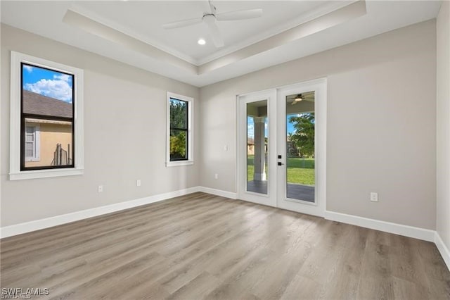 unfurnished room with french doors, ceiling fan, light wood-type flooring, ornamental molding, and a tray ceiling