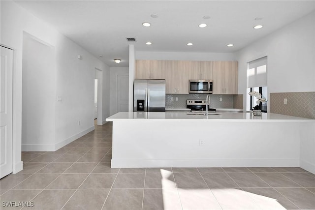 kitchen with kitchen peninsula, stainless steel appliances, sink, light tile patterned floors, and light brown cabinets