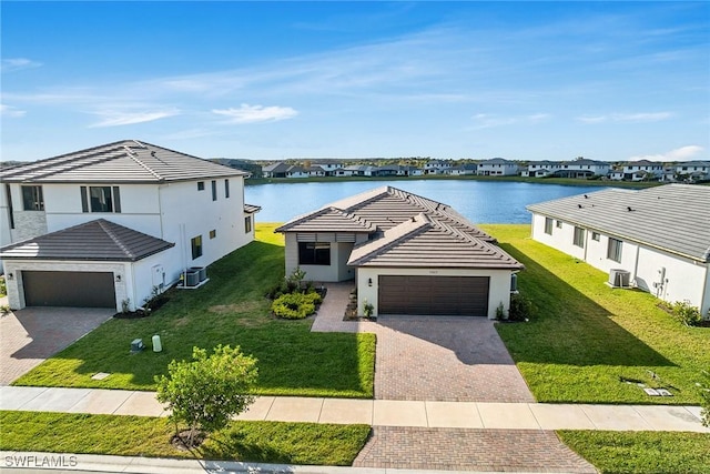 view of front of home featuring a front yard, central AC, a water view, and a garage