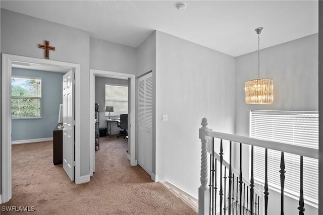 hall with light colored carpet and a notable chandelier