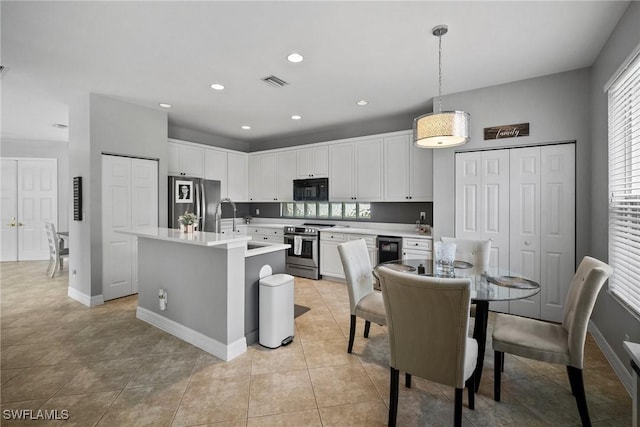 kitchen with white cabinetry, an island with sink, decorative light fixtures, light tile patterned floors, and appliances with stainless steel finishes