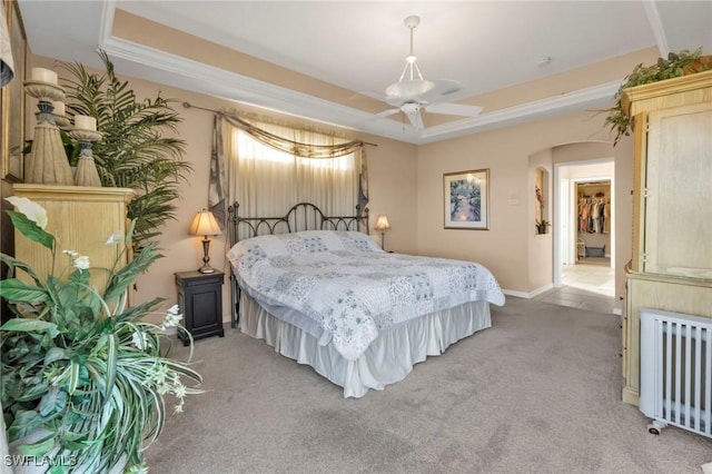 bedroom with radiator, ceiling fan, a tray ceiling, light colored carpet, and a closet